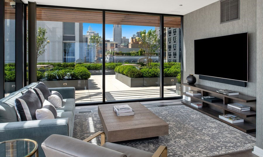 Club furniture and a coffee table site before a large television in the rooftop club at 61 Banks Street. The sky terrace can be seen outside the windows.