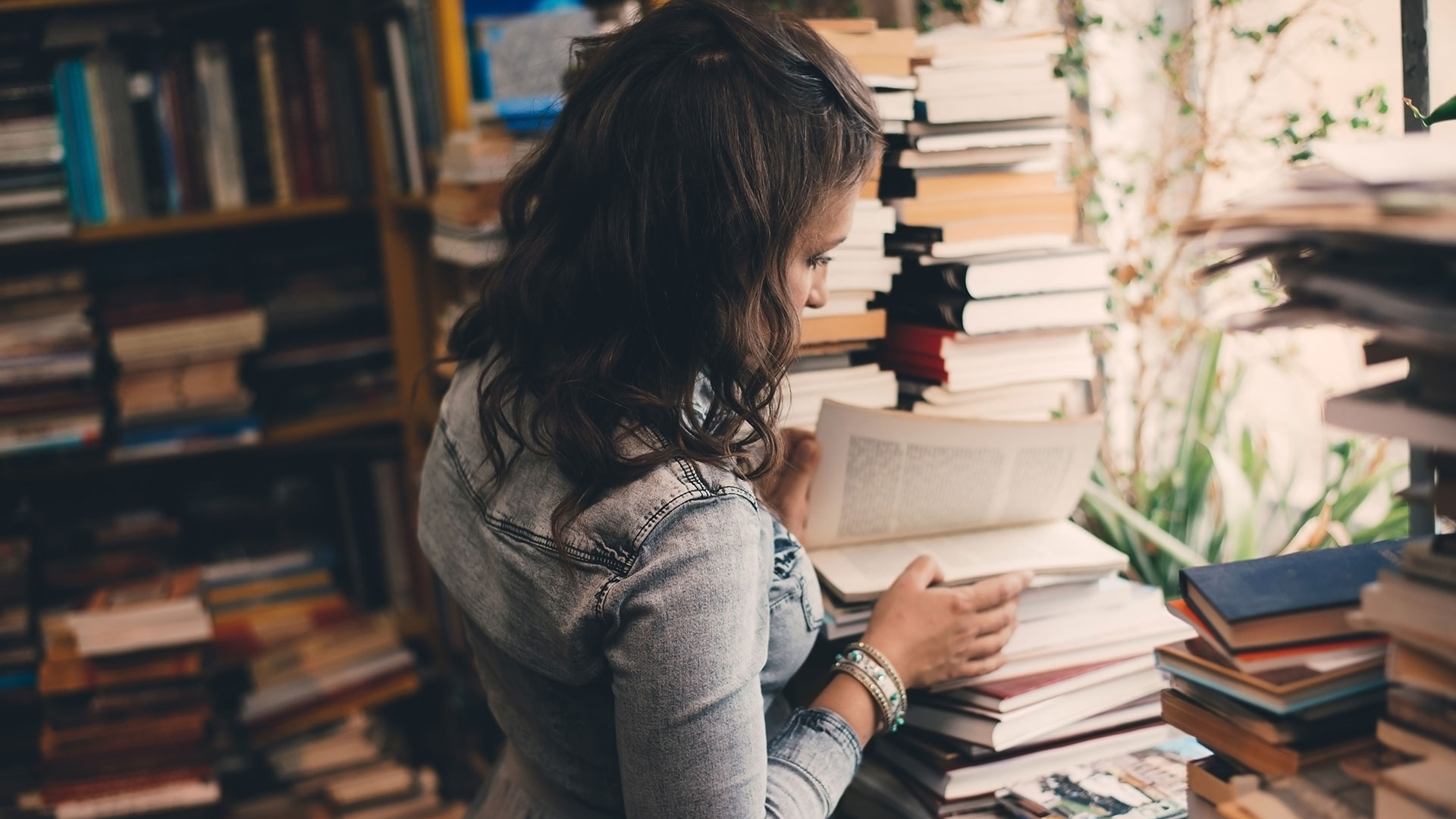 A woman stands with her back to us looking at a stack of books inside an old bookstore.