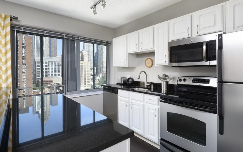 Chestnut Tower apartment kitchen with black countertops, stainless steel appliances, and downtown Chicago views