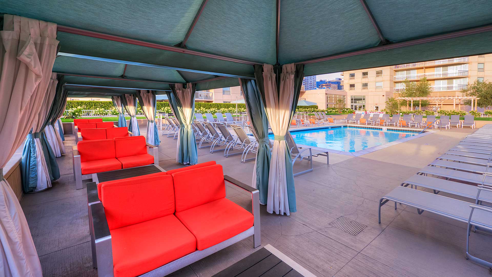 An image of couches in a row under several canopies beside the pool. The pool is seen in the background off to the left.