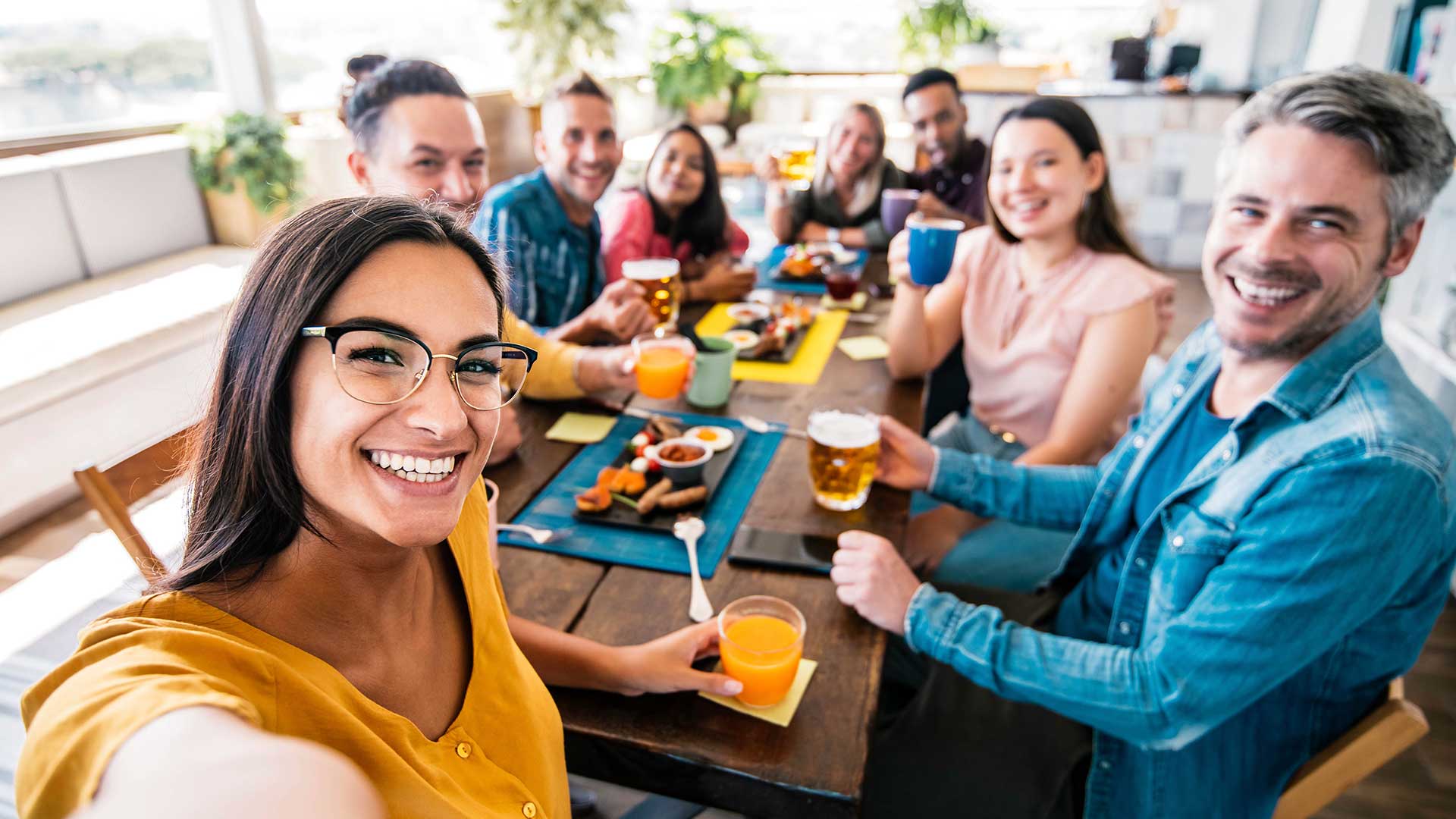 A group a friends smile to the camera while sitting around a table enjoying a meal.